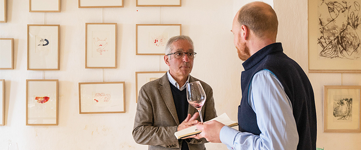 two men and a wine glass in front of a gallery wall
