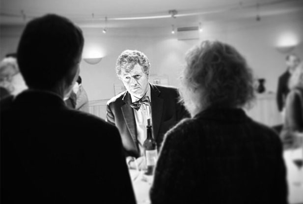 Black white, a man with a bottle of wine between the shoulders of two other people