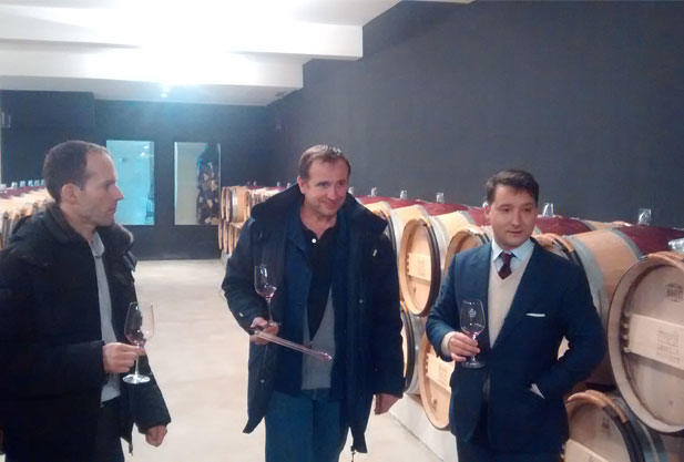 Three men amongst wine barrels with wine glasses