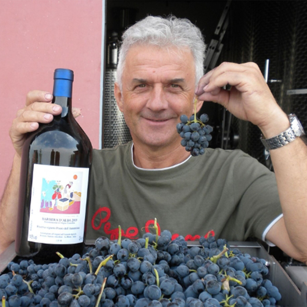 Roberto Voerzio holding a wine bottle beside grapes