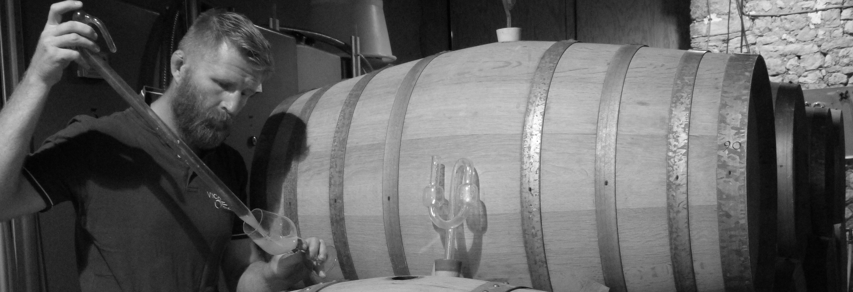 Man decanting into wine glass in front of cask