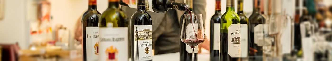 A table with six wine bottles and a glass of red wine being poured into