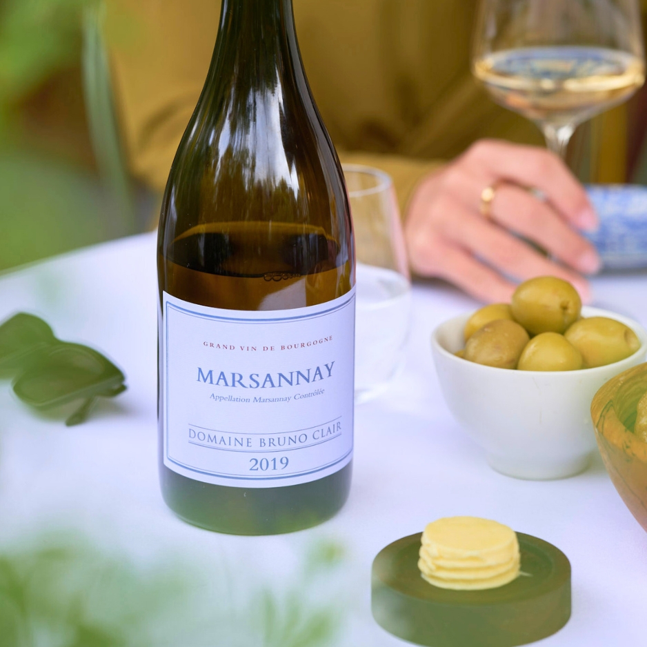 table with marsannay wine bottle and woman holding glass of white wine