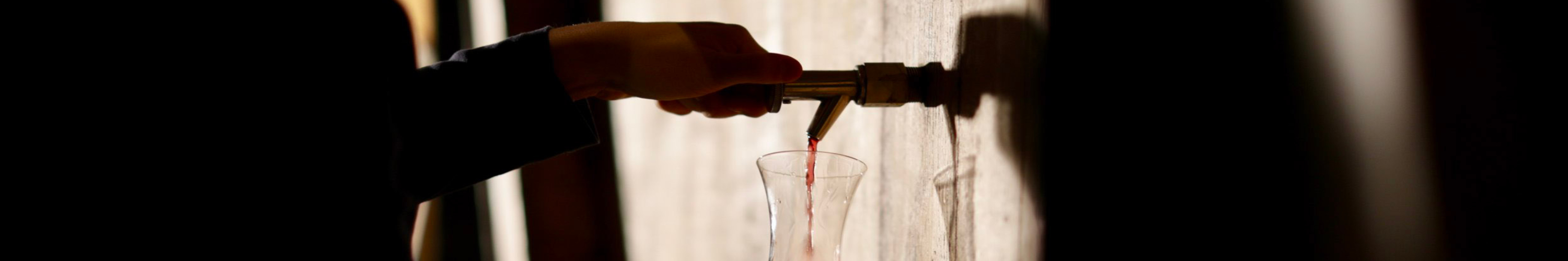 close up of hands pouring wine from a tap in a barrel
