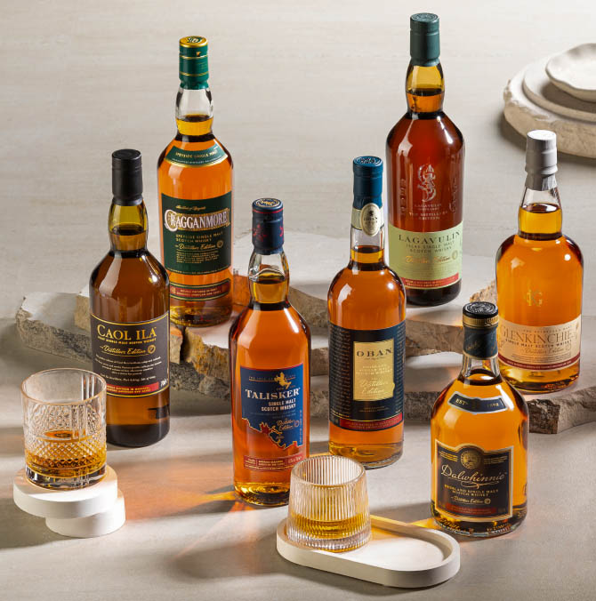 Seven bottles of varying whiskies on a table with two glass of whiskies