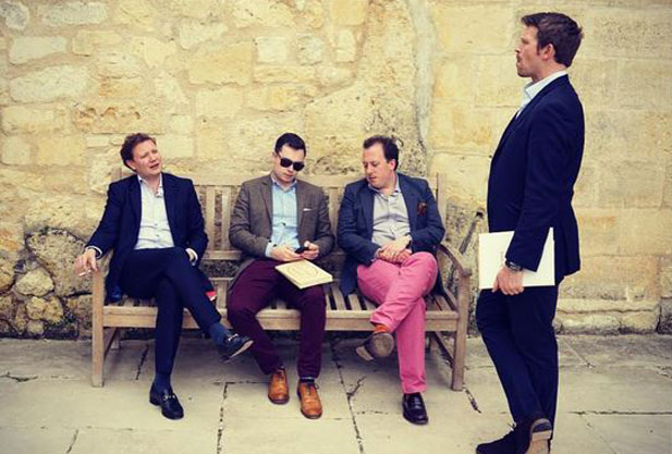 Three men sitting on a bench, one standing