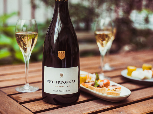 A bottle of Philipponnat on a bench with champagne glass and food
