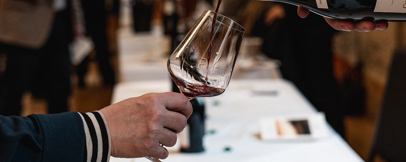 A glass being poured with red wine in a tasting event