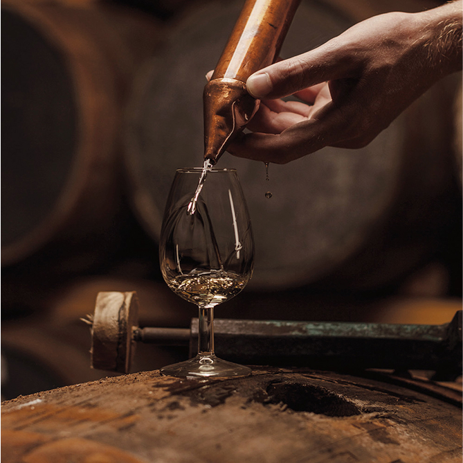 A glass being poured with whisky from a cask