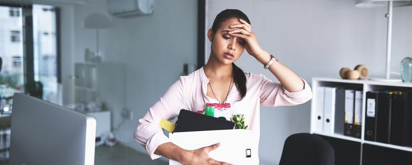 Woman in office holding files and placing hand to forehead
