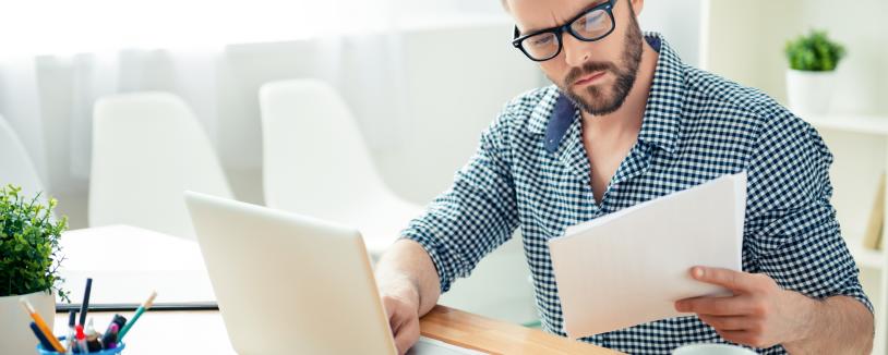 Man in glasses with laptop reading paperwork