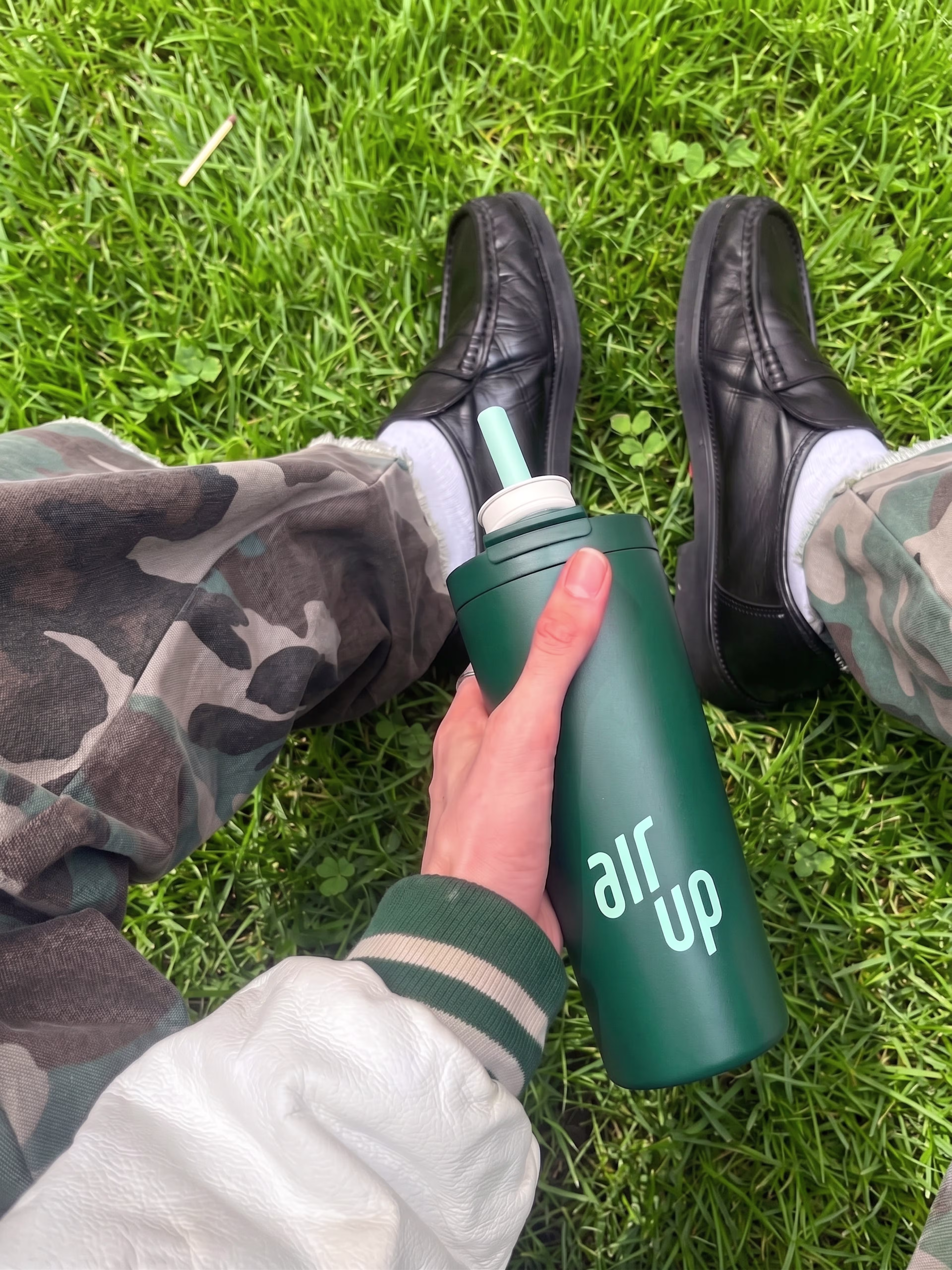 Hand holding a dark green air up bottle while sitting on grass