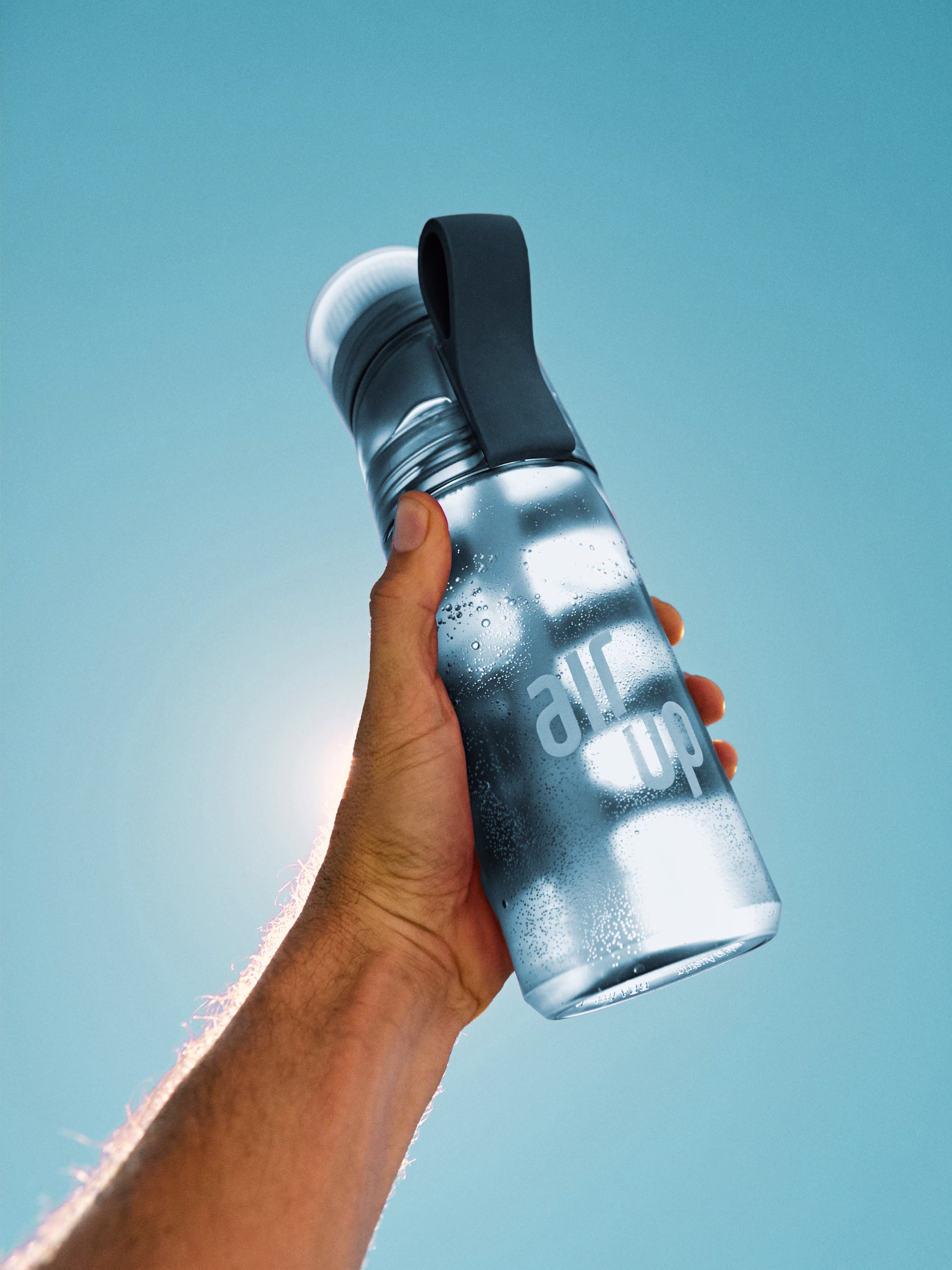 Hand holding up a frosted air up bottle against a bright blue sky