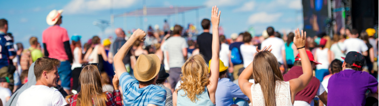 A crowd at a festival, blue skies, arms raised in the air 