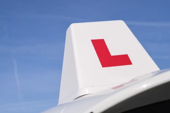 Close-up of a sign showing a red L on top of a driving instructor's car.