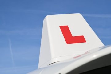 Close-up of a sign showing a red L on top of a driving instructor's car.