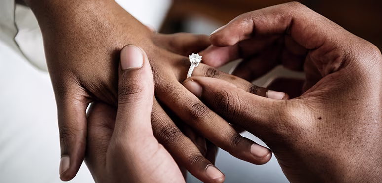 A man's hand placing an engagement ring onto a woman's hand.