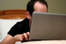 Close up of a man using a laptop, his face obscured by the screen.