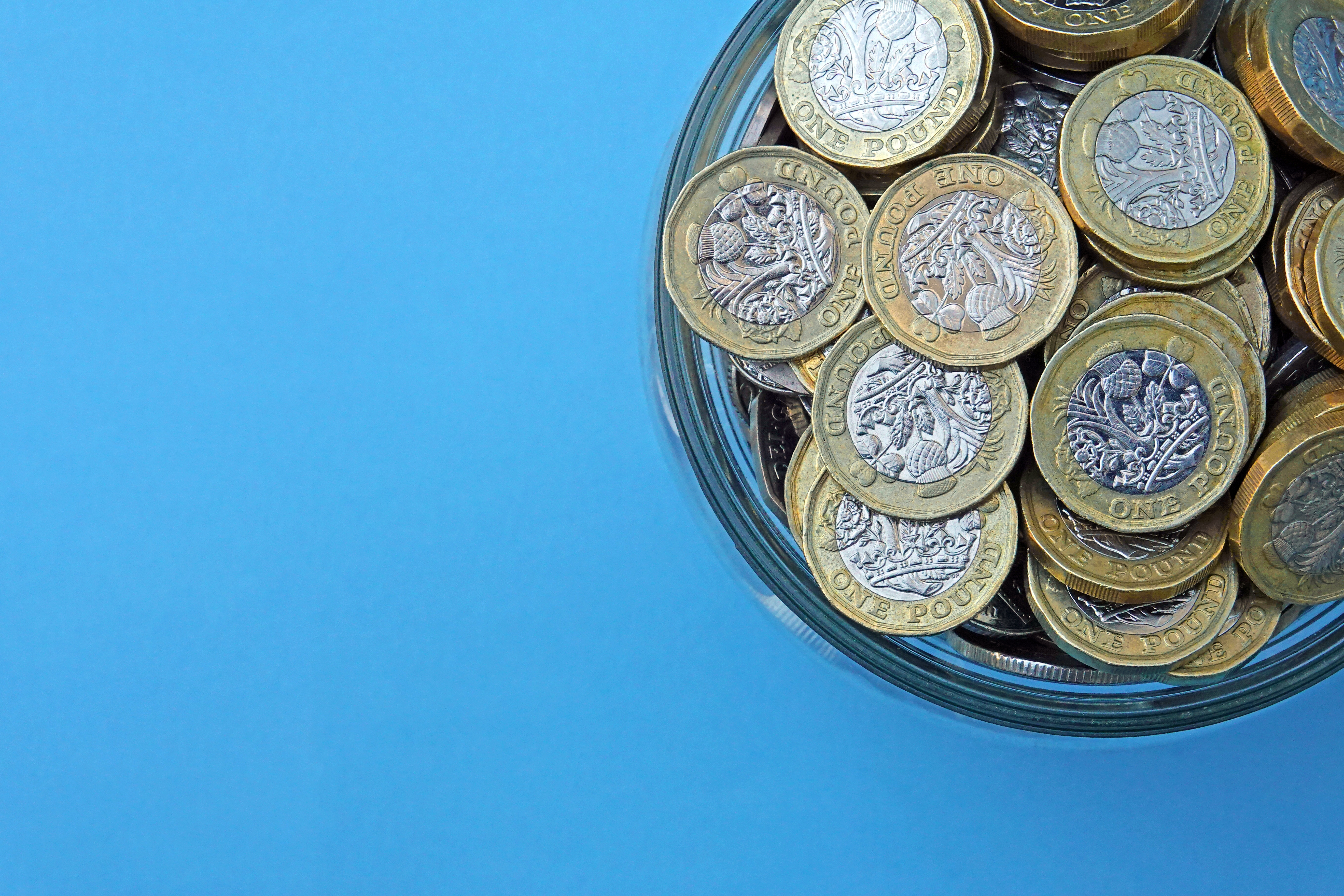 A jar of pound coins against a blue background.