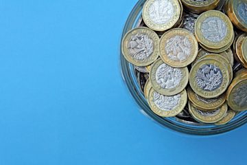 A jar of pound coins against a blue background.