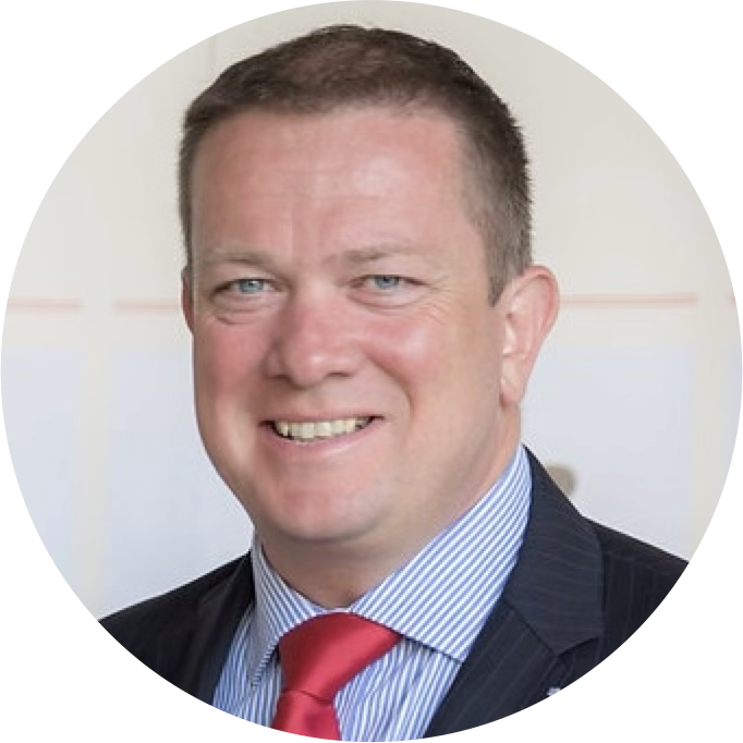 A headshot of a man wearing a dark suit, a blue shirt and a red tie