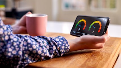 Person holding in-home display for energy smart meter in one hand and a cuppa in the other