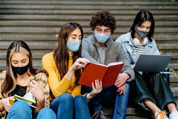 Four university students sitting on stairs, reading books and doing work on a laptop