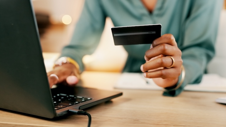 Woman holding a payment card and using a laptop