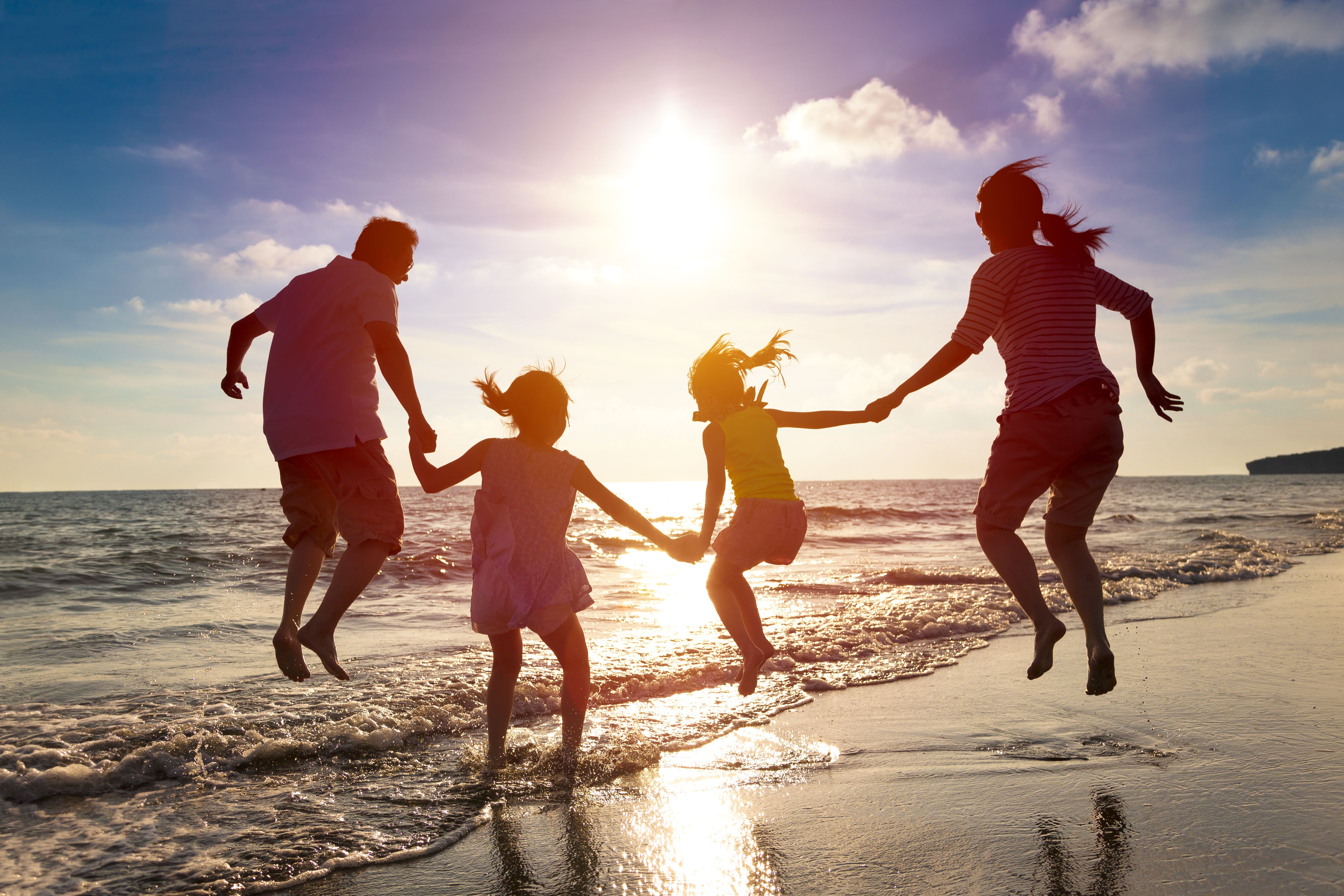 Silhouettes of a family running and jumping along the beach at the water's edge at sunset.
