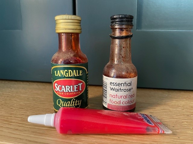 A bottle of Langdale Scarlett food colouring, a bottle of Essential Waitrose natural red food colour and a Dr. Oetker red food colour gel.