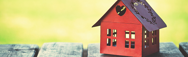 A red model of a house with a heart cut into the wall, sat on a wooden bench.