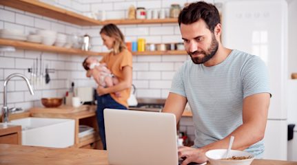 Dad on laptop in kitchen with mum holding baby nearby