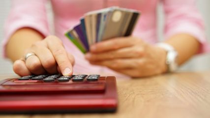 close up image of person holding several credit cards and using a calculator