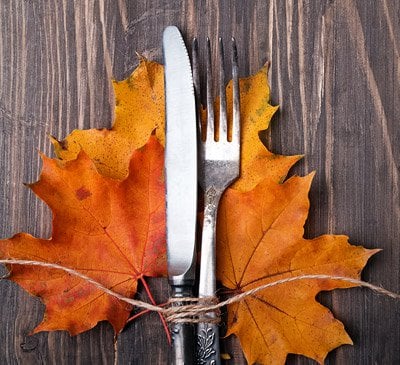 An autumnal cutlery place setting: a knife and fork tied to orange leaves.