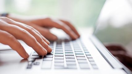 Close up of hands typing on a computer keyboard.