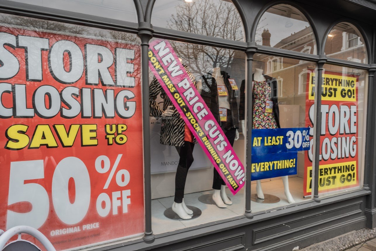 Four posters in a shop window, the biggest of which says "Store closing. Save up to 50%."