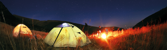 Photo of two dome tents in a field beneath a star-filled dark sky, with hills in the background.