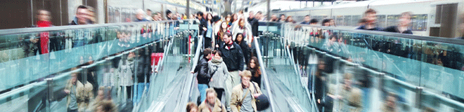 Photo of passengers moving along the platform and down an escalator in a train station.