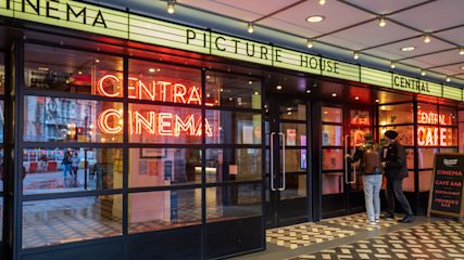 The front door of Picturehouse Central in London, with black-framed windows, a checkered floor, and neon red signs in the windows