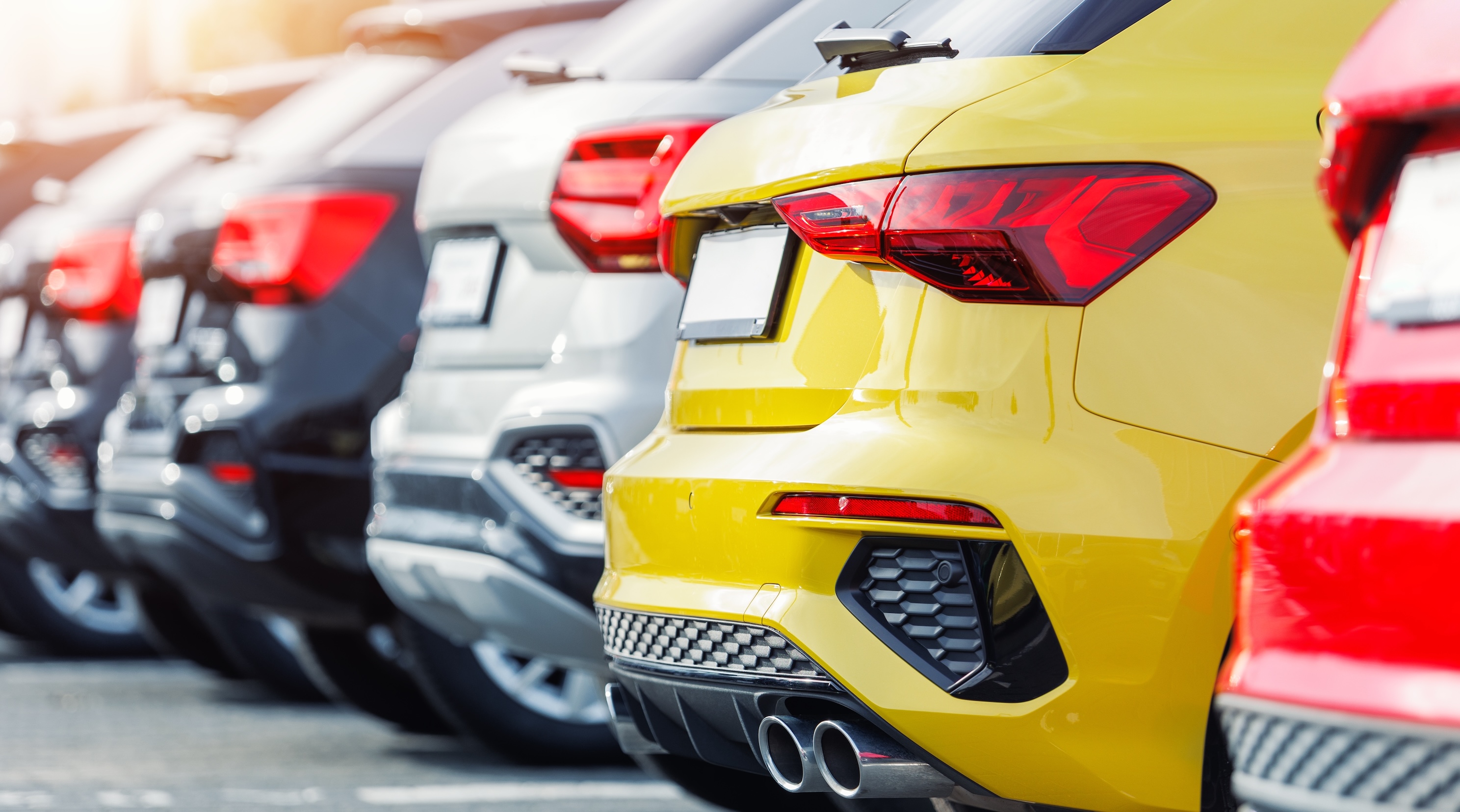 The backs of five different coloured cars all parked in a row. 