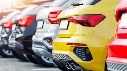 The backs of five different coloured cars all parked in a row.