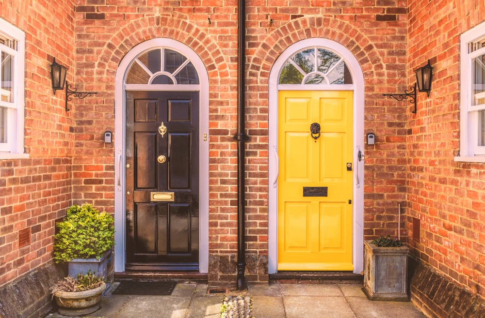 Two red-brick semis focused in on their two doors - the left is painted black and the right is painted yellow.