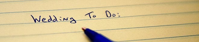 The tip of a pen on lined paper below 'Wedding To Do:" written on the page.