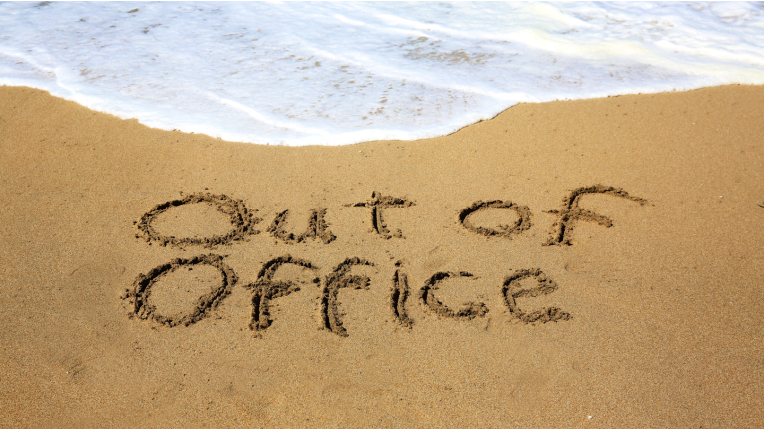 'Out of Office' written in the sand on a beach with the sea coming in at the top of the picture.