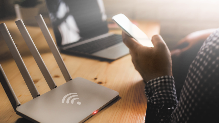 Person using their mobile and laptop next to a wifi hub. 