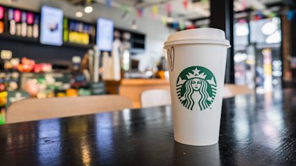 A white and green cup with the Starbucks logo sitting on a table in a coffee shop