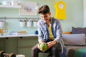 A young man holding a green piggy bank and smiling