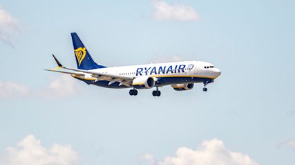 A Ryanair plane in flight against a pale blue sky