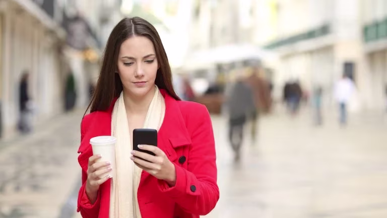 Woman on high street holding smartphone and takeaway coffee cup