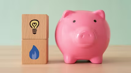 A pink piggy bank next to two wooden blocks, one with a light bulb drawn on, and the other with a blue flame